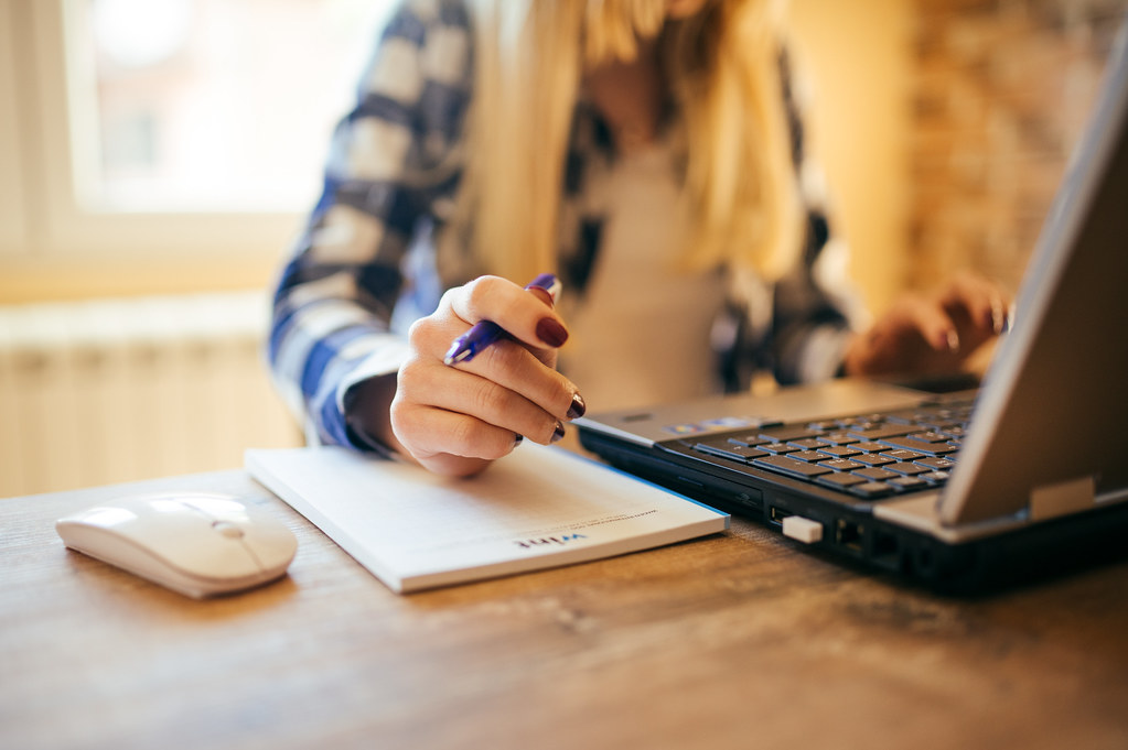 Professional taking notes with a pen while working on a laptop in an office